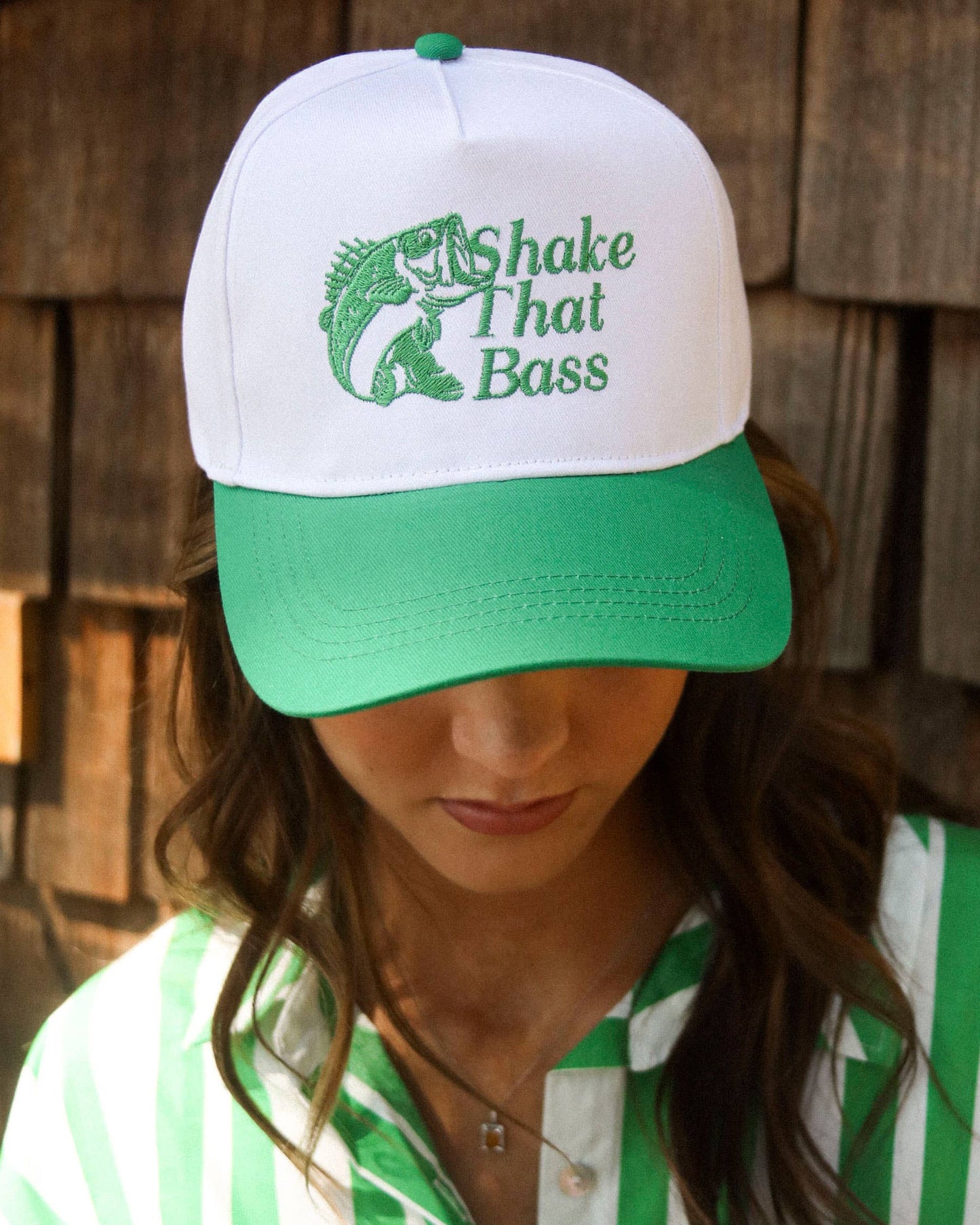 Person wearing a white and green cap with 'Shake That Bass' design against a wooden background