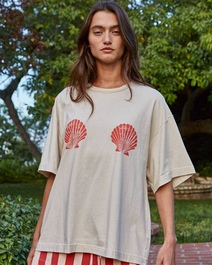 Woman wearing a beige t-shirt with red shell designs and striped shorts outdoors.
