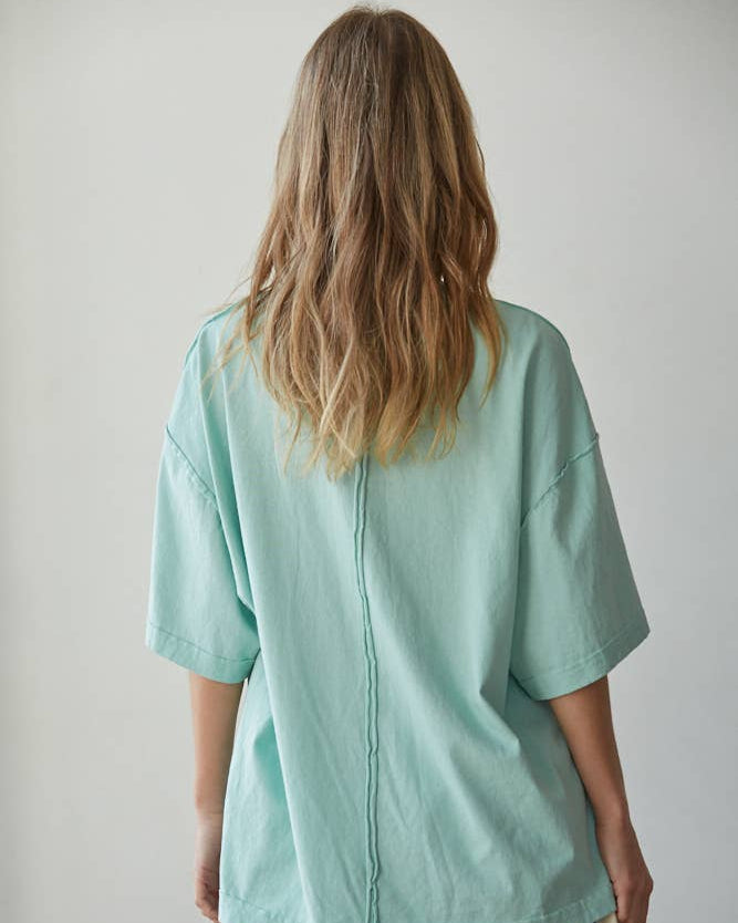 Person wearing a light green oversized shirt and striped shorts against a plain background