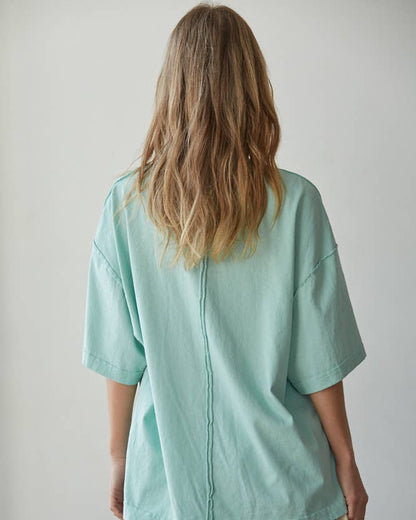 Person wearing a light green oversized shirt and striped shorts against a plain background