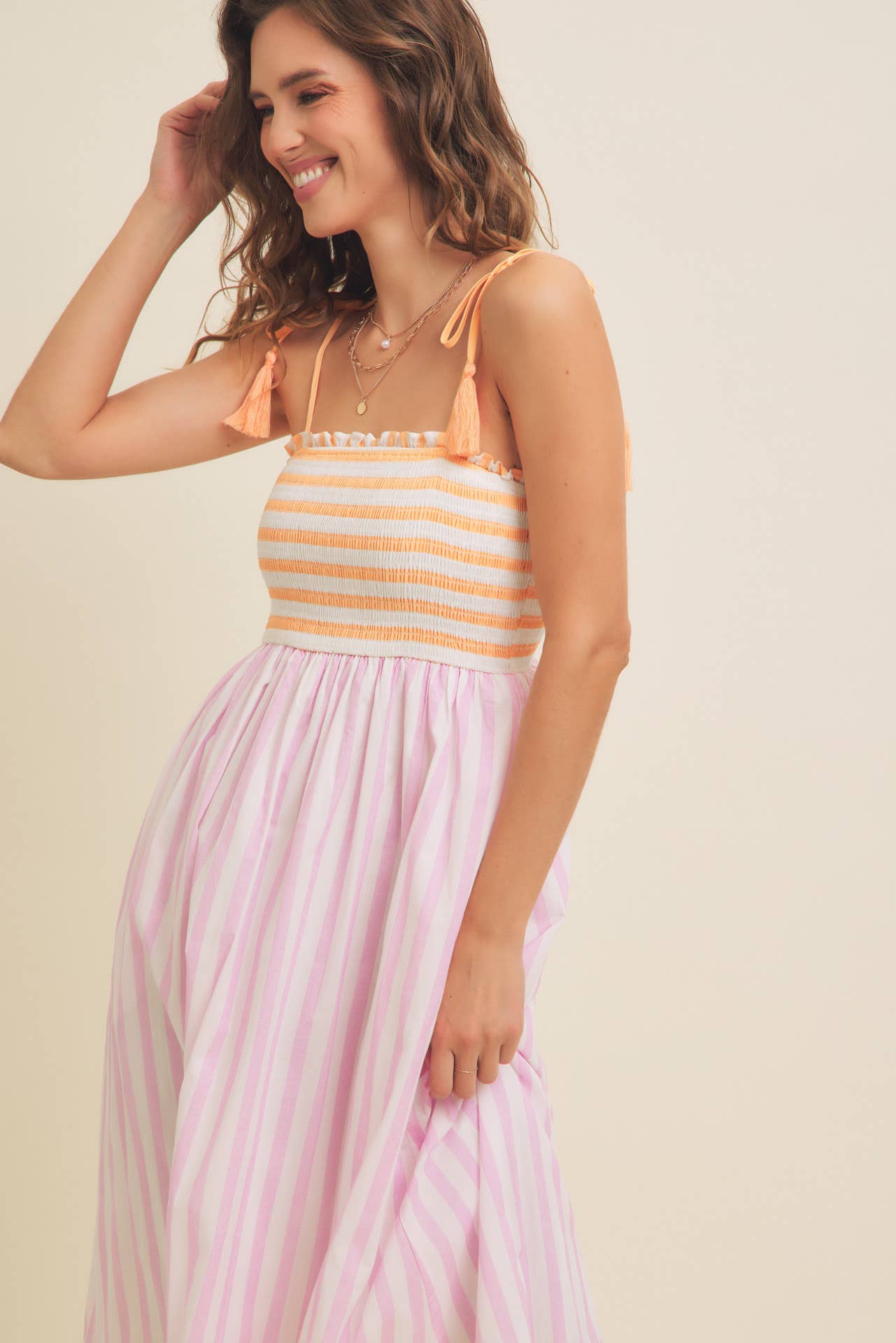 Woman wearing a pink and yellow striped dress against a beige background