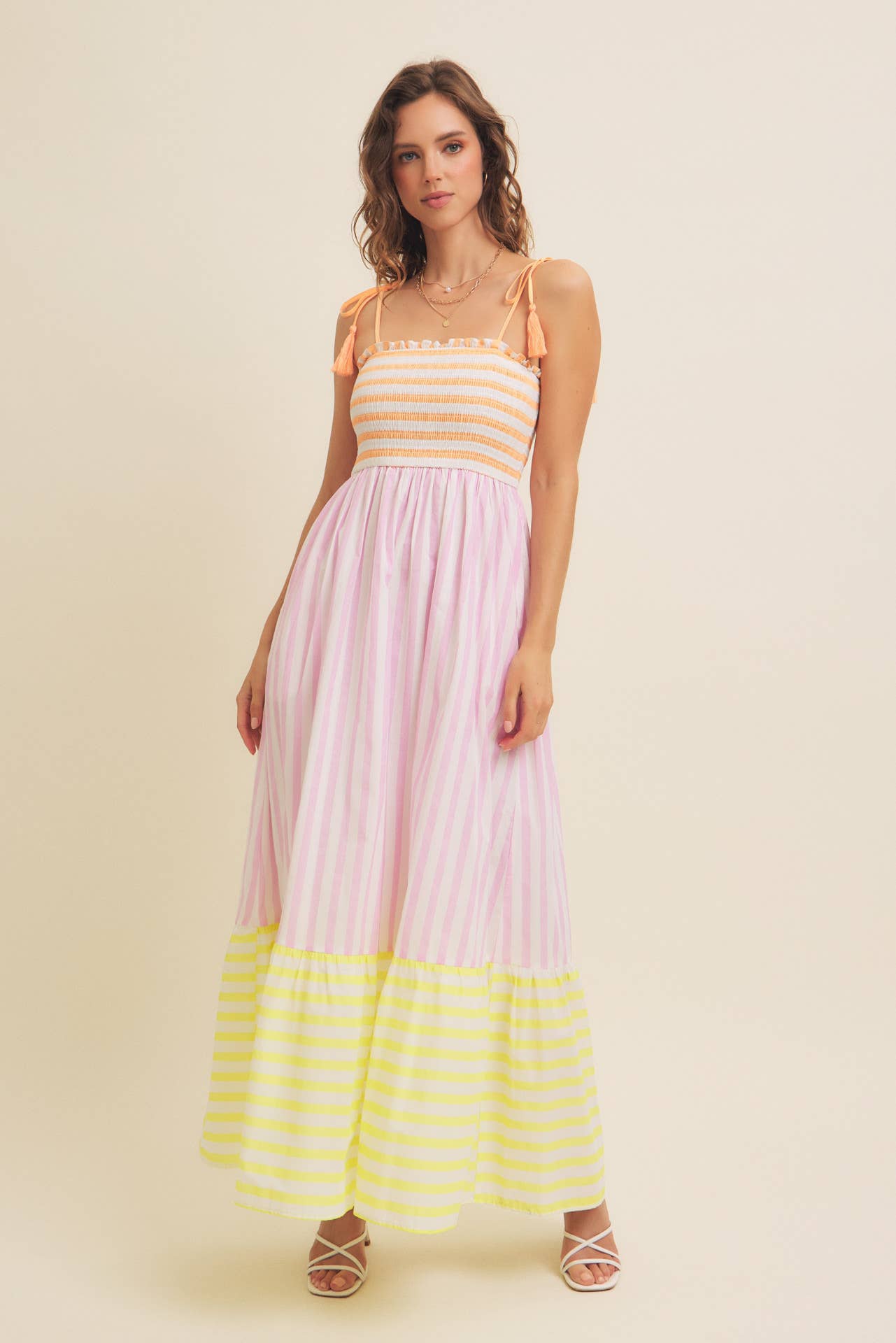 Woman wearing a striped dress with a yellow and pink color scheme on a beige background