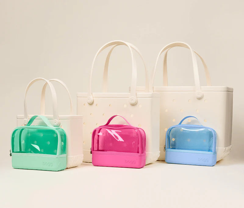 Set of three clear bags in green, pink, and blue with white handles on a light background