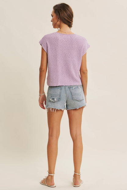 Woman wearing a light purple t-shirt and denim shorts on a beige background