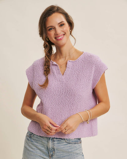 Woman wearing a purple knitted top and denim shorts on a plain background