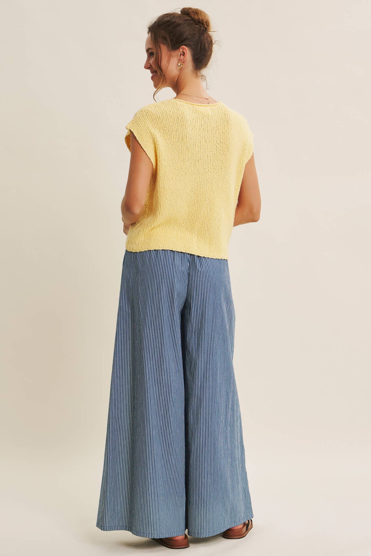 Woman wearing a yellow top and blue wide-leg pants on a beige background