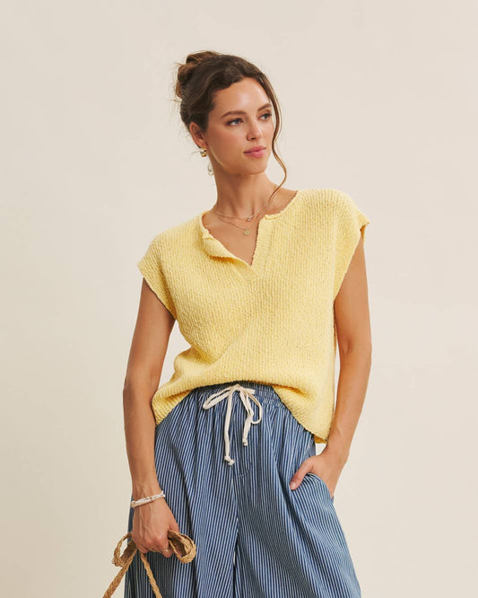 Woman wearing a yellow top and blue pants, holding a woven bag on a beige background