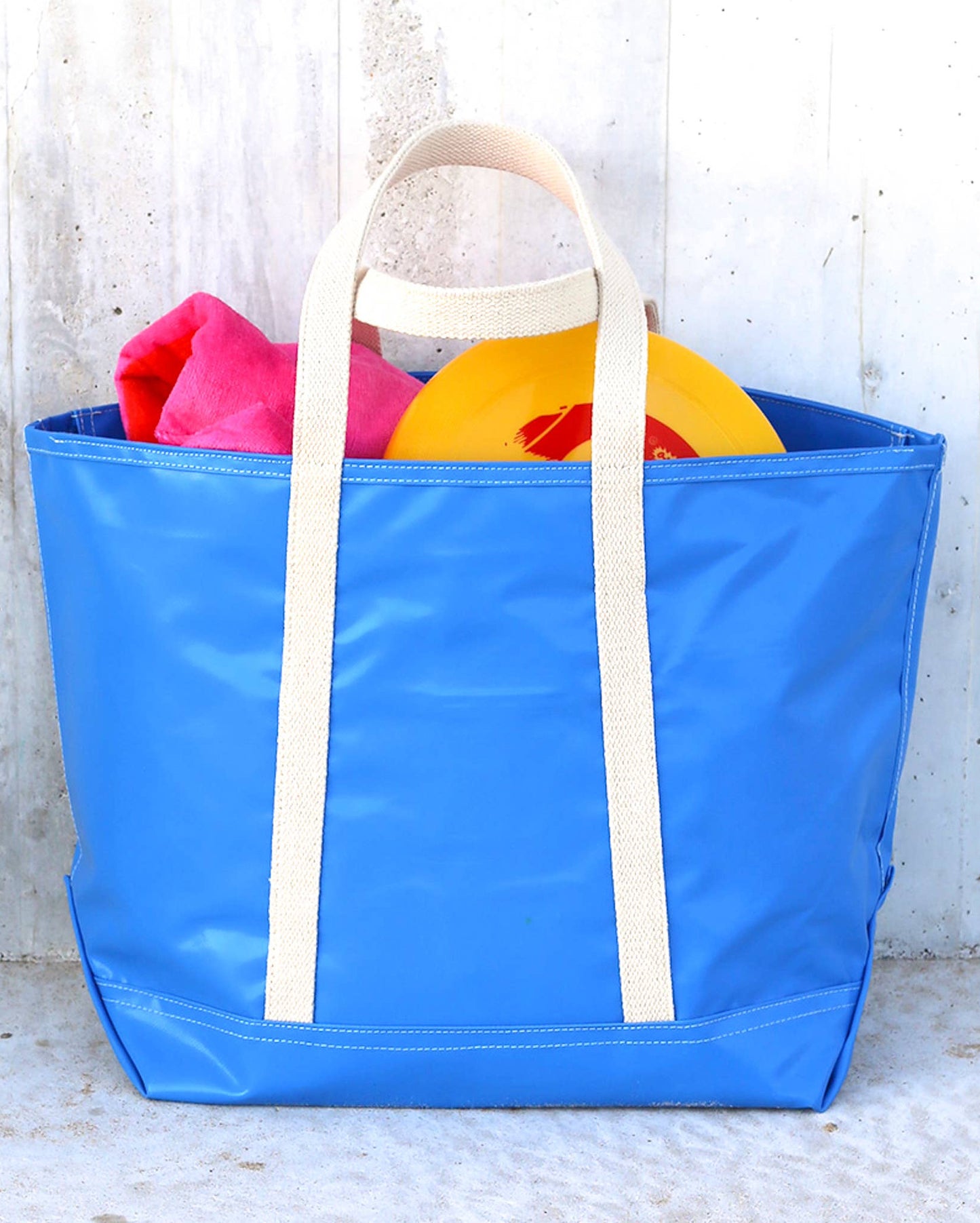 A blue tote bag with white handles and a zipper, displayed on a wooden surface.