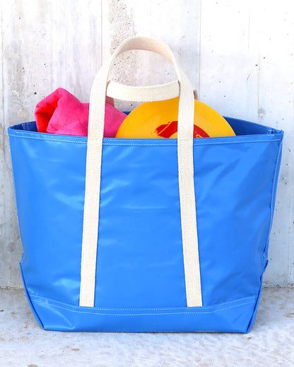 A blue tote bag with white handles and a zipper, displayed on a wooden surface.