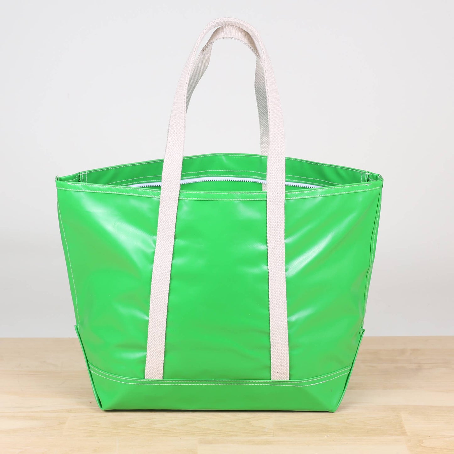 A green tote bag with white handles and a zipper, displayed on a wooden surface.
