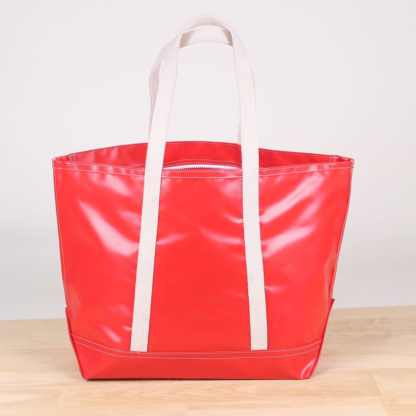 A red tote bag with white handles and a zipper, displayed on a wooden surface.