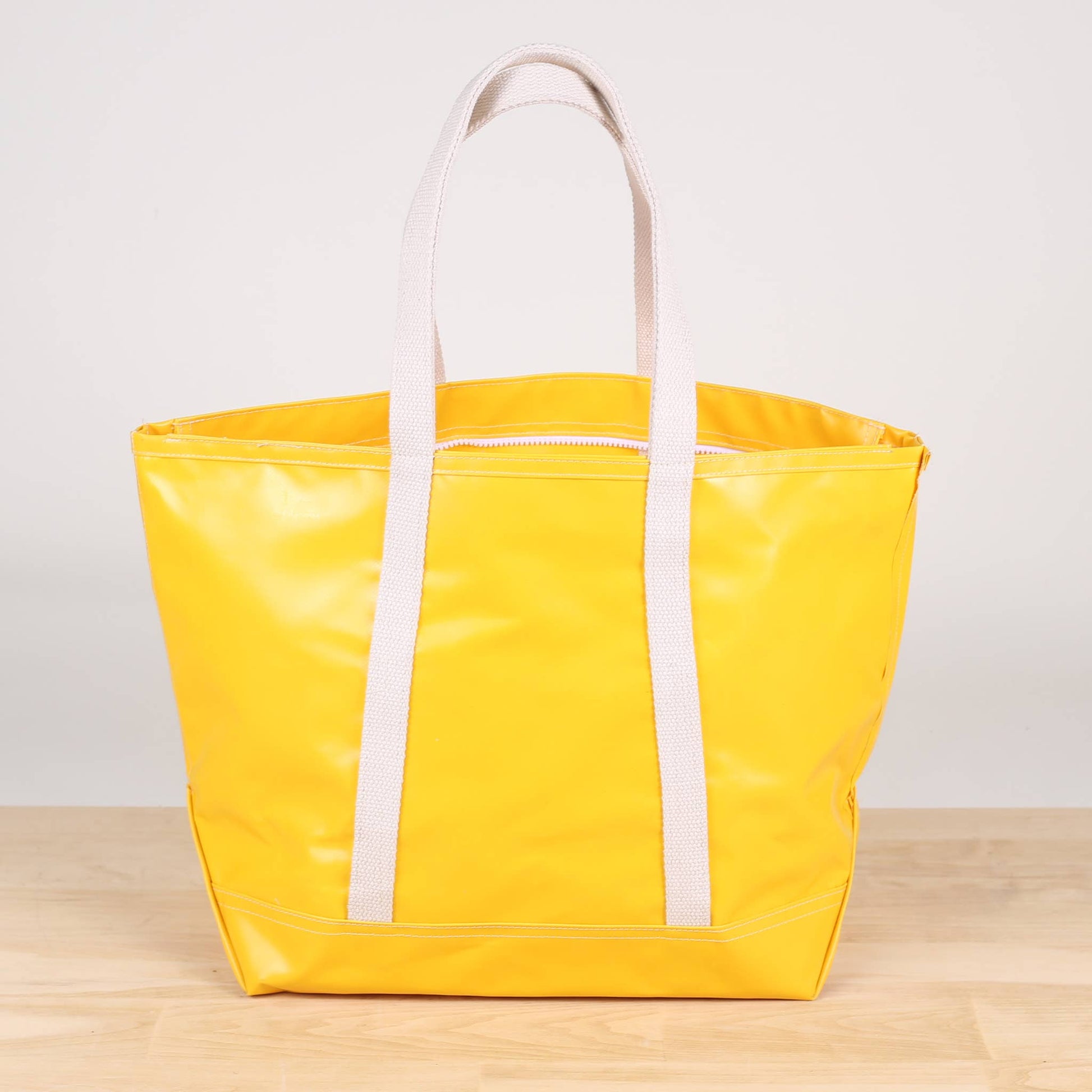 A yellow tote bag with white handles and a zipper, displayed on a wooden surface.