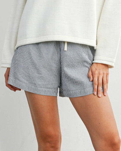 Woman wearing a white sweater with an American flag design, gray shorts, and black rain boots on a plain background.