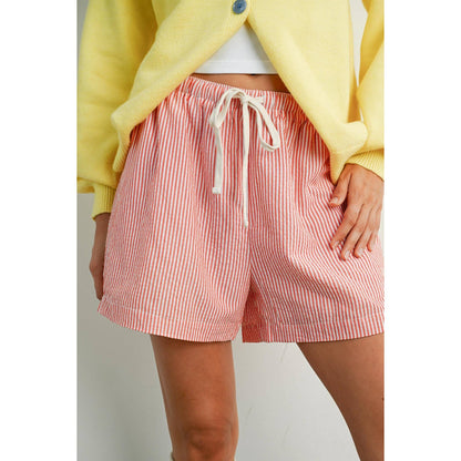 Person wearing red and white striped shorts with a yellow cardigan on a plain background