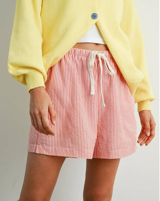 Person wearing a yellow cardigan and red and white striped skirt on a plain background