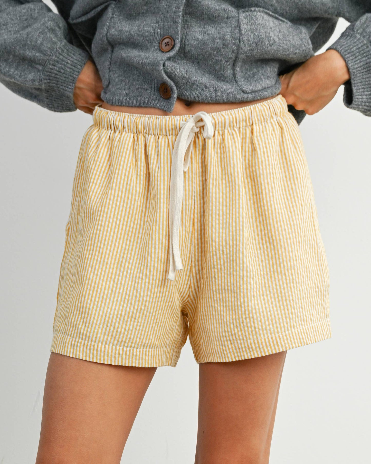Person wearing beige shorts and a gray sweater on a plain background