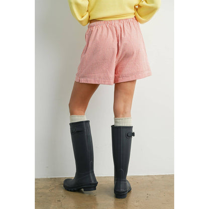 Person wearing pink checkered shorts and black rain boots on a plain background