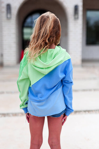 Person wearing a green and blue hoodie with a blurred background