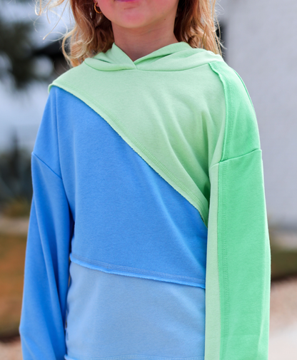 Person wearing a blue and green color-blocked hoodie with a blurred background