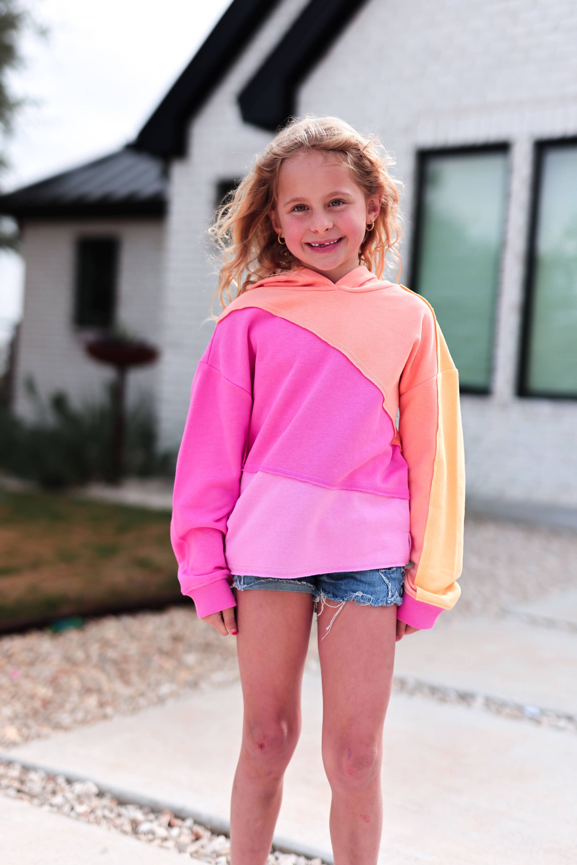 Young girl wearing a colorful hoodie standing in front of a house.