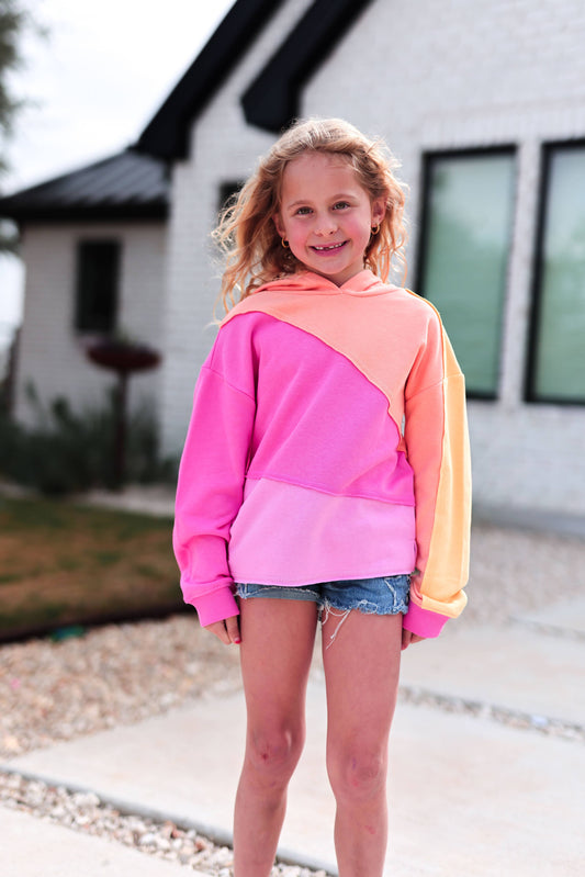 Young girl wearing a colorful hoodie standing in front of a house.
