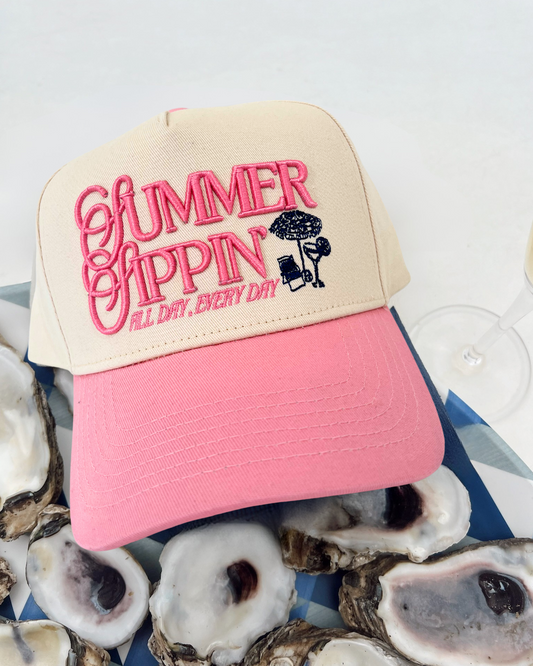 Pink and beige cap with 'Summer Shoppin' text on a background of oyster shells.